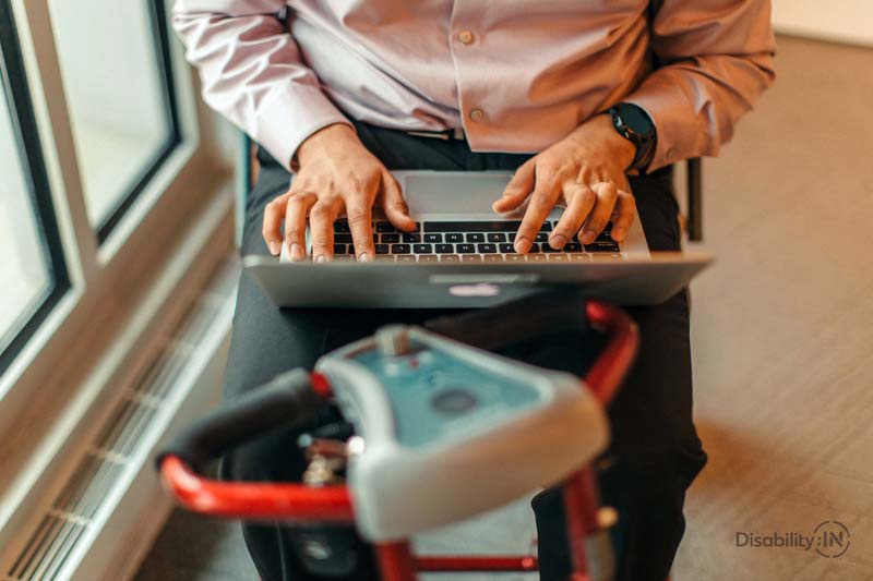 A man in a motorized wheelchair using a laptop.