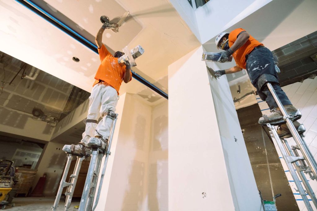 Two men on scaffolds applying joint compound to drywall